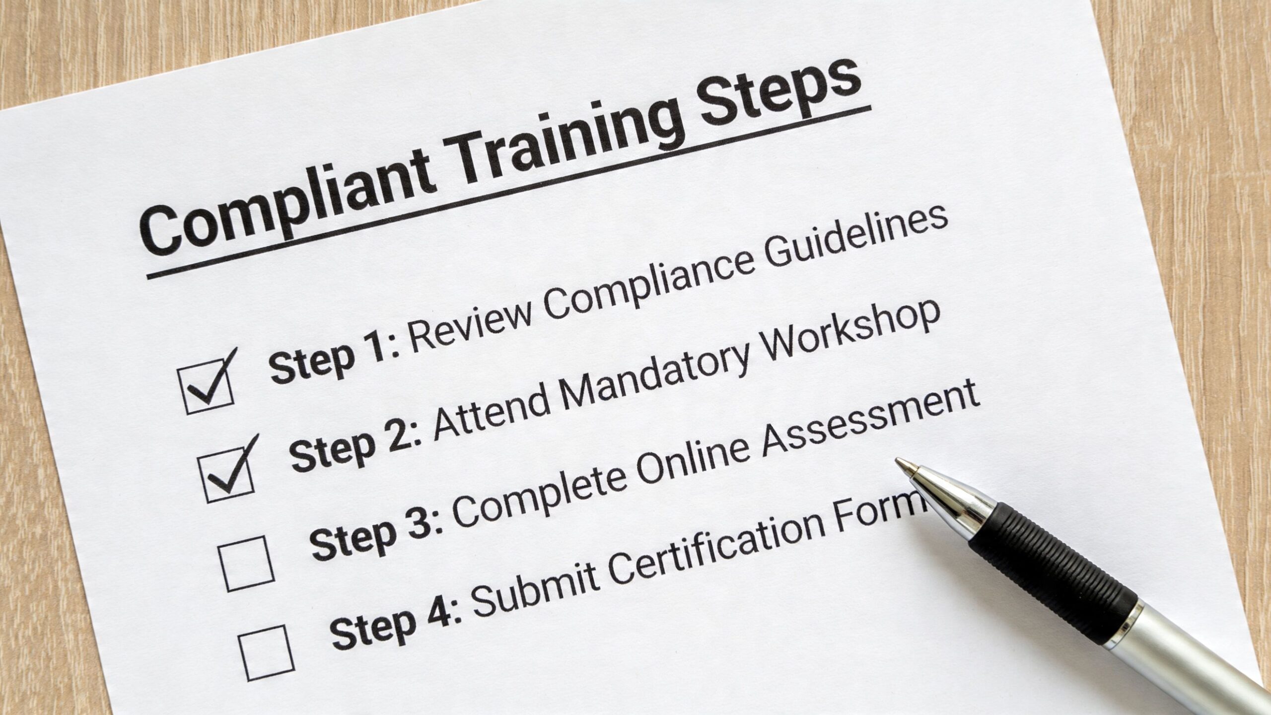 A checklist labeled Compliant Training Steps with two items checked off and a pen resting nearby.