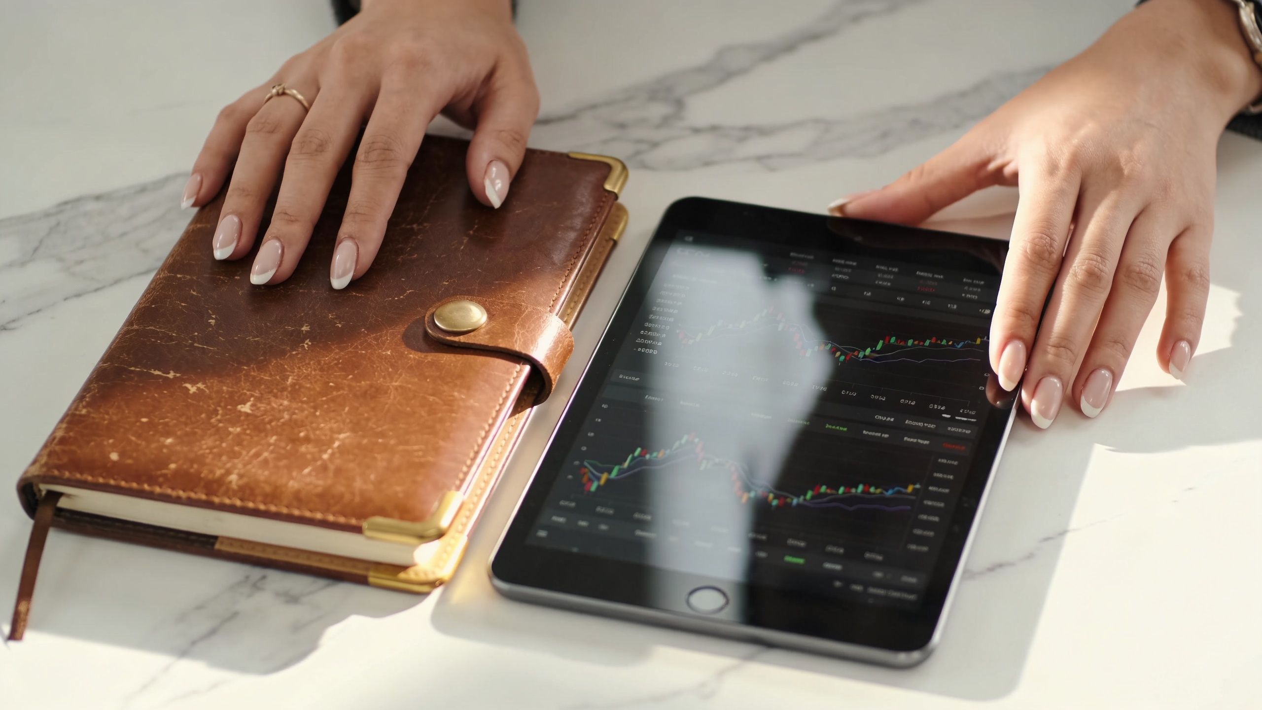 A professional analyzing stock market charts on a digital tablet next to a leather personal planner.